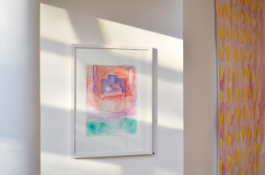 In the middle a framed watercolorpainting of a house, in red, violet and green. On the right a big painting with yellow shapes on a pink ground. Anna Slobodnik, 2018. 