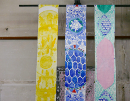 Upper part of three hanging canvases in yellow green and blue and a work on paper behind them. 