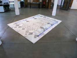 View of an assembled drawing of a carpet, lying on the floor between columns. 
