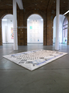 Exhibition view with a checkered assembled drawing on canvas lying on the floor. 