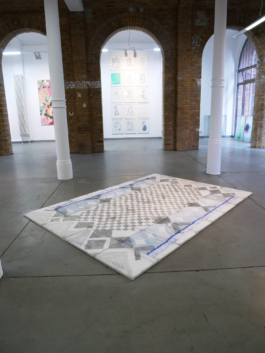 Exhibition view with a checkered assembled drawing on canvas lying on the floor. 