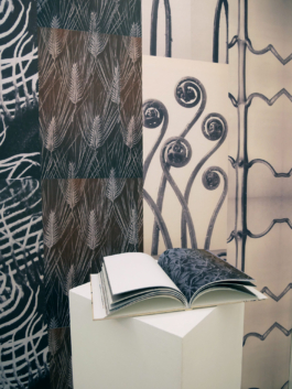 A book lying on a plinth in front of a patterned wall. 
