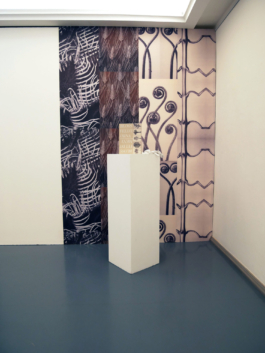 Floral wallpaper on the wall and infront of it a book with a floral cover on a plinth. 