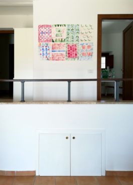 Room with two doors and a railing above the railing eight colorful watercolor painting of patterns. 