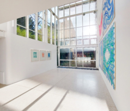 View of a sun room with framed stone prints in red, blue and green on the left and 4 big canvas paintings on the right. 