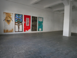 An exhibition space with five painted doors hanging on wall in the left corner. 