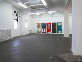 View of an exhibition space, paintings of doors in the back in the room a metal sculpture infront of them. 