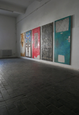 Picture of five paintings of doors hanging on the wall, seen from the right. 