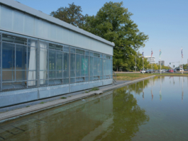 View on a road with a glass building, a water fountain and some trees. 