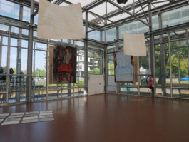 Two drawings on paper in front of two paintings of chairs one brown and one blue one. To the left there are works in concrete. 