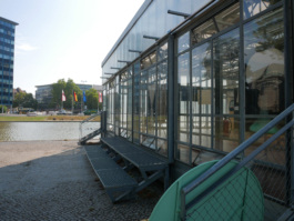 To the ride a building out of glass. To the front a water bassin and modern buildings behind it. 