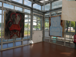 View of a corner of a glass building with two paintings of two chairs a brownish red one and a blue striped armchair. 