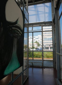 A painting of a green and black glass on the left, on the right view through a window on a street and some modern buildings and cars. 