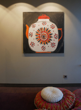 Painting of teapot with a red and orange pattern on black ground hanging on the wall. 