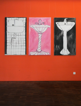 View of three paintings of sinks, two black ones and one pink one in the middle on a red wall by Anna Slobodnik. 