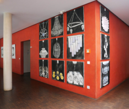 A red wall seen from the corner with 12 paintings of lamps hanging on it. 