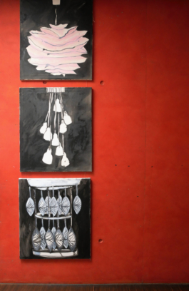 View of three paintings of lamps hung on top of each other on a red wall. 