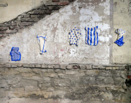 A demolished looking wall, on this wall there are five ceramic objects, which depict kitchen towels. 