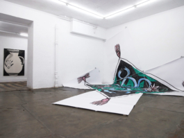 In a bigger room to on the right side there is a big painting on paper, showing a scarf, to the left we see a smaller room and a painting of a jug. 