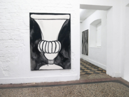 Exhibition view with one black and white painting of a vase and another in the background. 