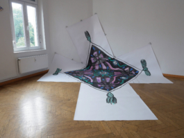 A painting of a quadratic scarf in ink, purple and turquoise on five pieces of paper partly on the floor and partly on the wall. 